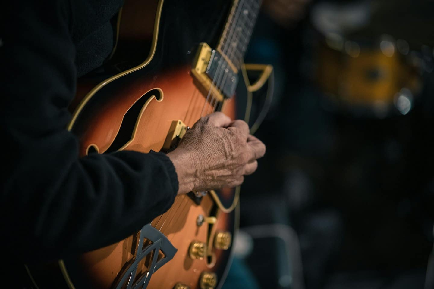 Una mano rugosa appoggiata su una chitarra elettrica archtop sunburst.