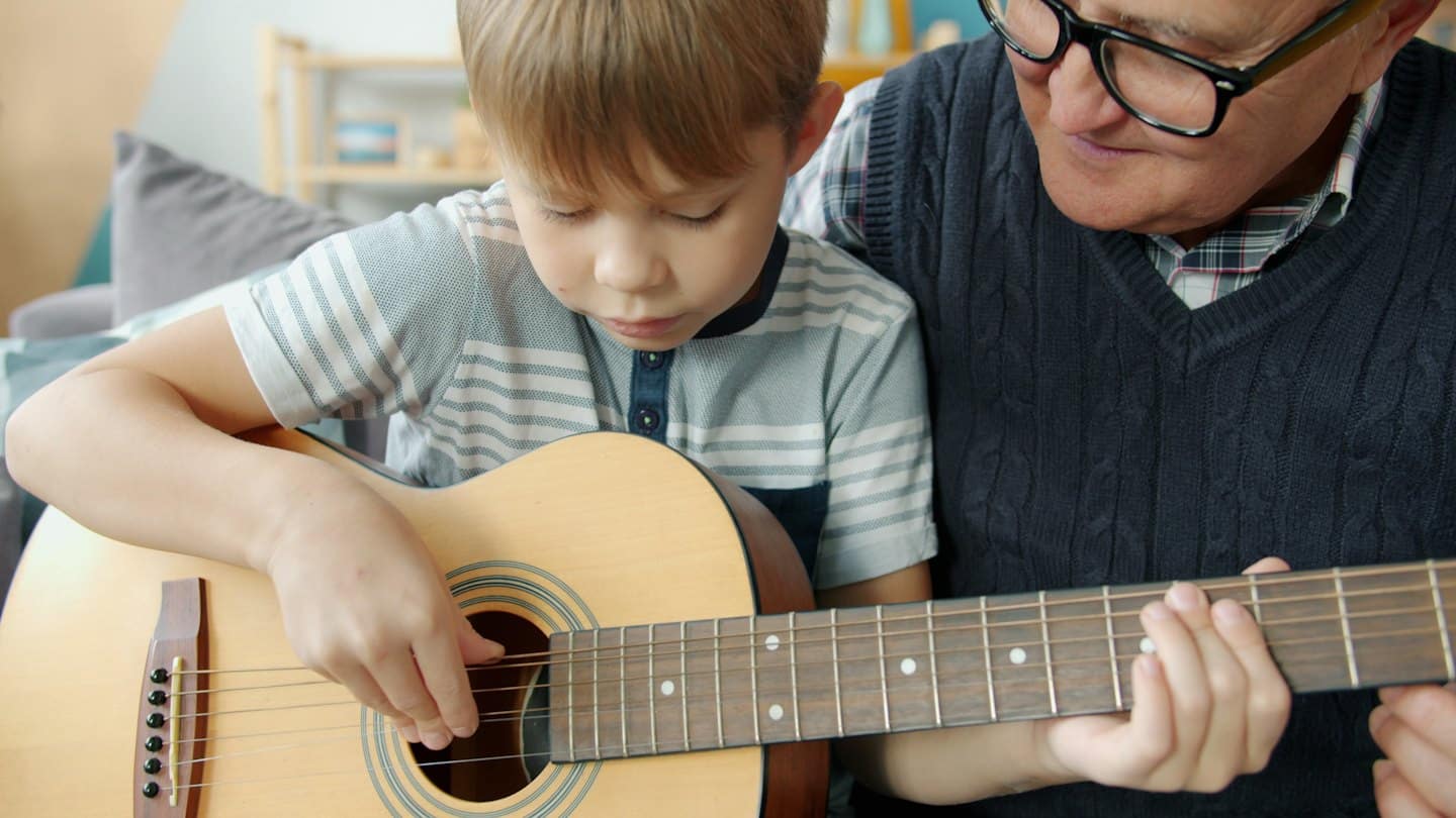 Un istruttore aiuta un ragazzo a suonare una chitarra acustica.